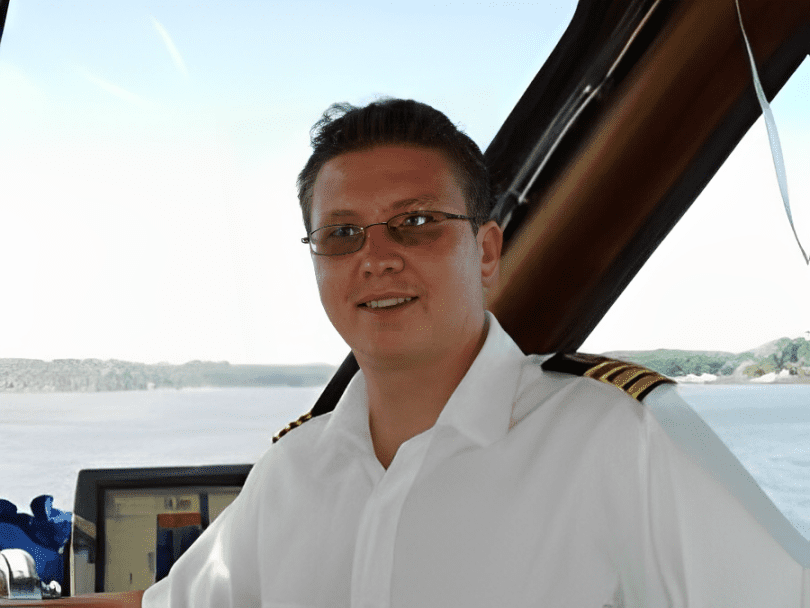 A man in white shirt and glasses standing next to a boat.