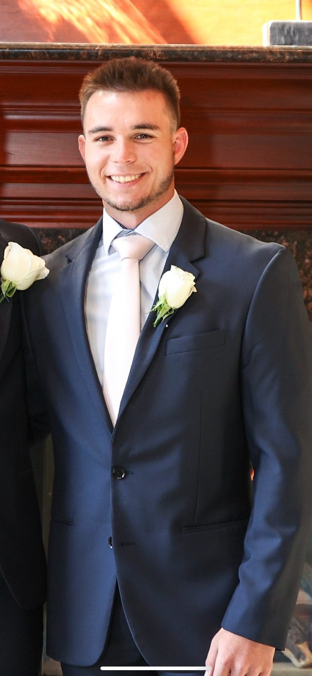Screenshot A man in a suit and tie with two white roses.