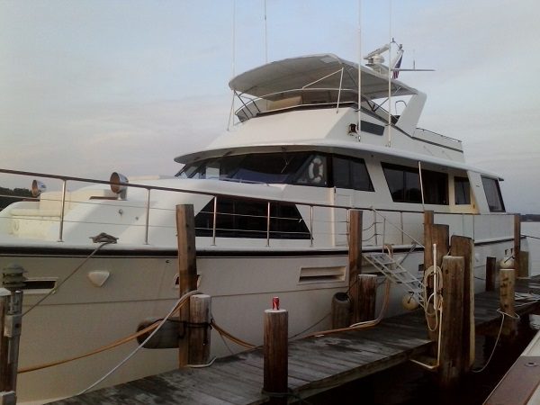 Laid-Off Large white yacht docked at a wooden pier, featuring multiple decks and windows, with mooring ropes secured to the dock.